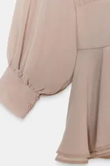 Vestido corto de tejido fluido en color beige rosado, con cuello subido ajustable mediante lazada en la espalda. Presenta mangas largas abullonadas con puños abotonados, cintura entallada y falda con bajo acabado en volantes. Incluye forro interior y cierre lateral con cremallera oculta.
