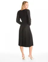 Vestido midi negro de seda fría con escote en V decorado con aplique de guipur y lazo central. Presenta mangas largas fluidas con puños fruncidos, hombros con leves frunces y cintura ajustable con lazo que da paso a una falda plisada.
