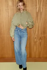 Jeans de tiro alto con diseño de pierna ancha y corte extra largo. Presenta una cintura cruzada asimétrica con cierre de cremallera y botones metálicos, además de un diseño clásico de cinco bolsillos.