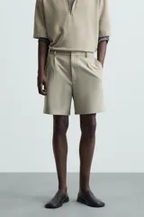 Bermuda de hombre color verde claro, de corte regular y tiro medio, con pinzas frontales, bolsillos laterales y bolsillos traseros de vivo. Cierre frontal con botón y cremallera.