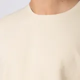 Remera oversized de algodón grueso con textura micropanal, color beige, de cuello redondo y manga corta, con costura decorativa en "X" en el escote y diseño liso sin logos.