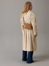 Bandolera Calvin Klein color tostado, con correa ancha de tela con logo de la marca y correa fina de cuero sintético.