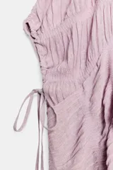 Top blanco de cuello redondo y mangas tipo capa, con textura fruncida, bajo asimétrico, lazos decorativos en el escote y en los laterales, y cierre posterior con botón.