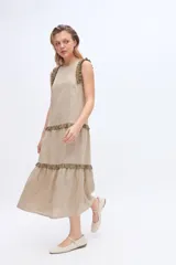 Vestido maxi beige de lino y algodón, sin mangas, con silueta relajada y escalonada. Presenta microvolados en verde militar que enmarcan los hombros y recorren los cortes horizontales de la falda.