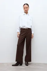 Camisa blanca de corte holgado, con cuello clásico, cierre frontal de botones y dos bolsillos delanteros con solapa.