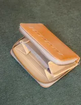 Billetera de cuero color tostado con cierre de cremallera. Interior con seis compartimentos para tarjetas y un compartimento para monedas con cierre. El billete entra doblado.