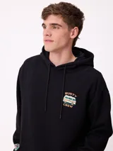 Canguro negro con capucha y estampado grande en la espalda de un paisaje con árboles, una camioneta camper y un lago al atardecer, con el logo "RUSTY" en la parte superior.