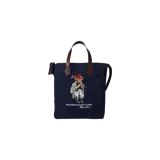 Bolso tote bag azul marino de lona con asas de mano y detalles en cuero marrón. Cuenta con un gran estampado central del icónico Polo Bear vestido de jugador de polo con casco rojo, acompañado del texto bordado "POLO BEAR by RALPH LAUREN".