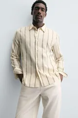 Camisa de corte relajado confeccionada en tejido mezcla de algodón, con diseño de rayas verticales, cuello solapa, manga larga con puños abotonados y cierre frontal de botones.
