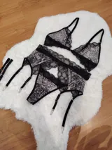 Conjunto de lencería compuesto por corpiño triangular, bombacha tipo colaless y portaligas, confeccionado en encaje negro con estampado animal print.