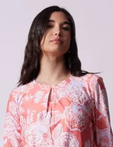 Blusa color salmón con estampado floral blanco, cuello redondo con abertura y mangas 3/4 acampanadas.