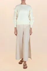 Suéter de punto color blanco, con cuello redondo, mangas largas abullonadas y detalle de volantes en los hombros y antebrazos.