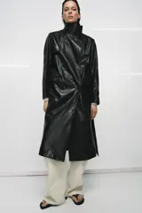 Trench de corte largo confeccionado en piel 100% con acabado brillante. Presenta cuello alto, hombreras marcadas, manga larga, bolsillos con solapa en el delantero y cierre frontal con botones. Incluye un cinturón ajustable del mismo material para entallar la silueta.