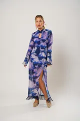 Vestido largo con estampado abstracto en tonos azul, lila y blanco. Tiene cuello mao con abertura en forma de lágrima, mangas largas acampanadas, espalda abierta, tajo frontal y flecos en el ruedo.