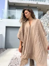 Ruana tejida en color beige, con diseño de trenzas verticales y terminación de flecos en el ruedo. Presenta una caída holgada y abierta al frente.