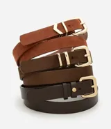 Set de tres cinturones de ancho medio con hebillas metálicas doradas. Incluye dos modelos con acabado de gamuza sintética en tonos marrón claro y oscuro, y un modelo de cuero sintético liso en color marrón muy oscuro.