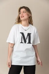 Remera blanca de algodón con cuello redondo, mangas cortas y estampa de la letra M en el frente. Incluye cadena plateada en el cuello.