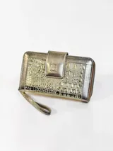 Billetera de cuero dorada con textura de cocodrilo, cierre perimetral y solapa frontal con broche magnético y detalle de búho grabado. Incluye tira de muñeca.