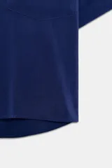 Camisa de cuello solapa y manga corta con dobladillo, presenta bolsillos de plastrón en el frente, bajo asimétrico y cierre frontal con botones ocultos.