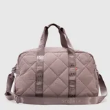 Bolso deportivo tipo duffel color negro con diseño acolchado de rombos. Cuenta con correas de mano y correa de hombro ajustable, ambas con el logo de la marca y coordenadas geográficas impresas. Incluye cierre principal y etiqueta pequeña lateral.