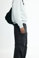 Pantalón cargo gris oscuro de corte holgado, con cintura elástica y bolsillos laterales, traseros y tipo cargo con solapa y botón a presión.