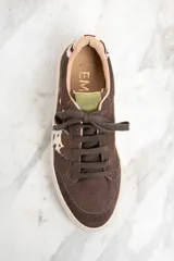 Zapatillas bajas de gamuza color marrón con cordones y suela de goma color crema. Presentan una franja lateral con estampado de vaca y el logo de la marca bordado en el lateral.