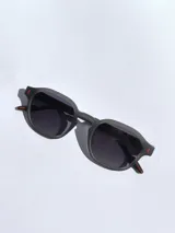 Lentes de sol con armazón de marco completo en color gris mate, con detalles decorativos en color rojo en las esquinas y patillas. Cuentan con cristales oscuros polarizados con protección UV 400.