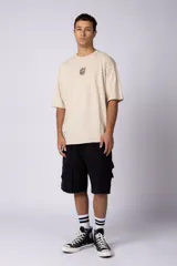 Remera oversize de corte holgado, color blanco, con cuello redondo y mangas cortas. Presenta un pequeño estampado circular en el centro del pecho con un diseño abstracto inspirado en arrecifes.