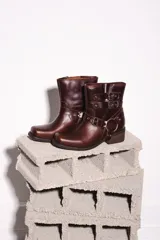 Botas cortas de cuero color marrón óxido con hebillas y arnés metálico.