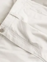 Pantalón cropped holgado color crema, confeccionado en sarga de algodón regenerativo. Presenta cintura plisada, cierre mediante botón y cremallera, bolsillos de hendidura y bolsillos traseros ribeteados.