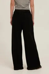 Pantalón negro de felpa ligera con tiro alto, corte relajado y pernera ancha. Cuenta con cintura elástica con cordón ajustable, bolsillos delanteros amplios con bordes sin rematar y detalles de costuras visibles.