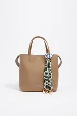 Pañuelo tipo twilly diseñado como charm para bolso, con estampado floral e ikat en tonos azul, verde, amarillo y naranja sobre fondo blanco. Incluye un anillo metálico plateado en forma de corazón que sujeta el pañuelo.