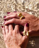 Anillo de diseño orgánico y macizo con forma irregular, elaborado en metal con acabado brillante. Presenta una estructura abierta que permite su ajuste.