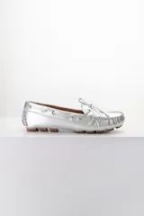 Mocasines plateados de cuero con cordones decorativos y suela de goma marrón.