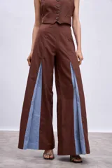 Pantalón largo color marrón, de corte ancho y tiro alto, con aberturas frontales en las piernas que revelan paneles internos en tono celeste.