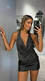 Top halter negro con acabado brillante y efecto drapeado en el escote. Presenta un diseño sin mangas con espalda descubierta y ajuste en el cuello.