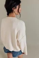 Cárdigan de silueta oversized confeccionado en hilo de algodón, color beige. Presenta escote en V, cierre frontal con botones, hombros caídos y mangas largas amplias con terminaciones acanaladas.