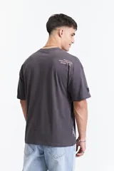 Remera de manga corta color gris oscuro, con corte holgado, hombros caídos y escote redondo. Presenta un logo estampado en el pecho con la inscripción "GALLERY DEPT." en color naranja.