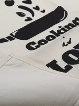 Delantal color natural con estampado de una olla y la frase "Cooking is Love".