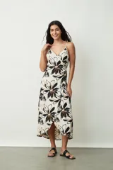 Vestido midi de tirantes finos, con escote en V y diseño cruzado estilo pareo. Presenta un estampado floral grande en tonos negros y naranjas sobre base off-white.