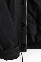 Campera de sarga levemente acolchada con cuello inglés, cierre frontal y solapa con botones. Presenta mangas raglán, bolsillos insertados delanteros, un bolsillo interior y cordón ajustable en el bajo.