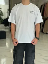 Remera oversize color beige, con diseño estampado en la espalda que incluye tipografía grande y texto descriptivo en negro.