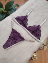Conjunto de lencería compuesto por un bralette triangular y una bombacha tipo tanga, confeccionados en encaje color violeta con terminaciones y breteles en color tostado.