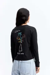 Remera de manga larga color negro, con silueta levemente boxy y largo a la cintura. Presenta una estampa lineal de una flor en el centro del pecho.