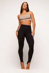 Calza legging de tiro alto color negro, confeccionada en tejido técnico de poliamida y elastano. Presenta un diseño minimalista con ajuste al pie mediante tira elástica (estribo).