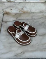 Zuecos negros de cuero con suela gruesa, detalle de tira de gamuza con hebilla metálica plateada y logo "AMÉN" estampado en la plantilla.