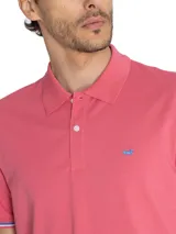 Chomba de piqué color rosa con cuello clásico y tapeta de dos botones. Tiene mangas cortas con puños acanalados con detalles de líneas blancas y azules. Presenta un logo bordado en el pecho.