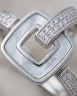 Anillo de acero con diseño de hebilla cuadrada que incluye incrustaciones de nácar y circonias en la banda.