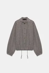 Chaqueta de manga larga con estampado de cuadros vichy en tonos marrón y blanco, cuello camisero, cierre frontal con botones y bajo ajustable con cordón.