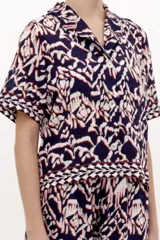 Camisa azul marino de manga corta, con cuello solapa, cierre frontal de botones y diseño estampado de estilo ikat en tonos blancos, rojos y azul marino.